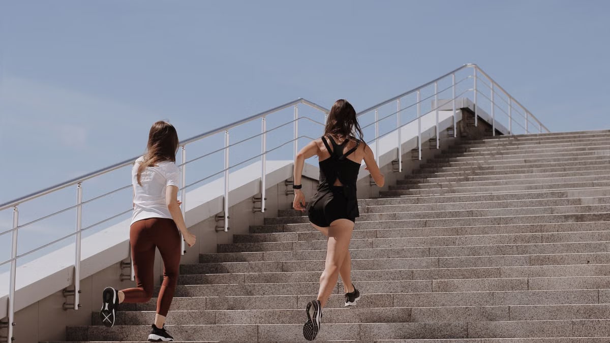 Two women running up stairs outdoors, embodying fitness and wellness.