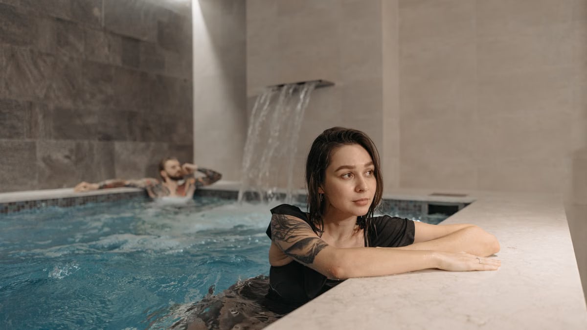 Tattooed woman and man enjoying a modern indoor pool setting, emphasizing relaxation.